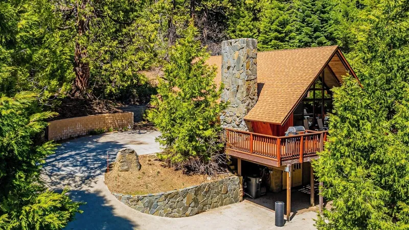 Half Dome Hideaway from above: its roof and stone chimney, the deck, and the driveway among the pines