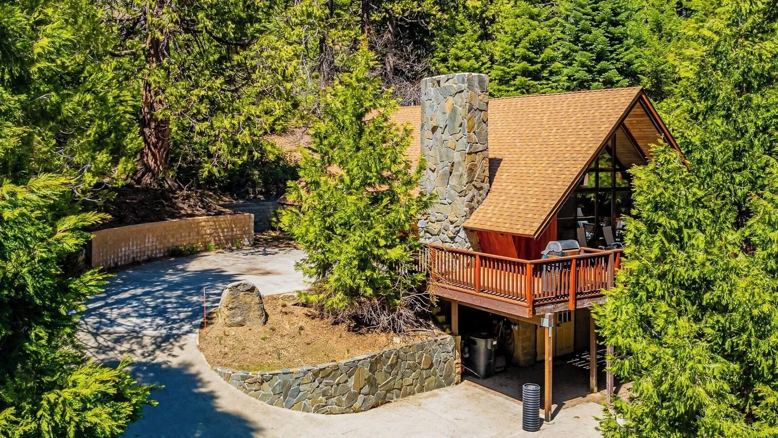 Half Dome Hideaway from above: its roof and stone chimney, the deck, and the driveway among the pines